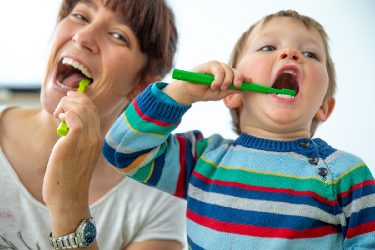 Parent and child looking into camera, happily brushing teeth
